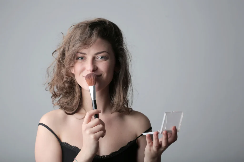 Uśmiechnięta kobieta używa pędzla do makijażu w studio, podkreślając urodę kosmetykami.